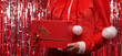 © Dimid - A woman in a red new years suit on a red background holds a gift box with a big red bow.