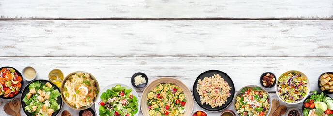 Fototapete - Variety of delicious homemade salads. Top down view bottom border on a white wood banner background. Summer food concept. Potato, caesar, pasta and green salads.