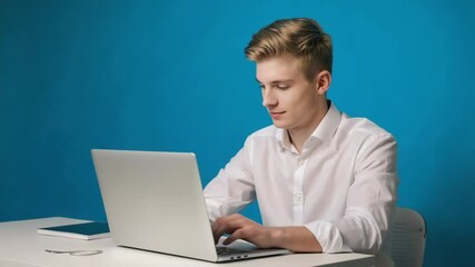 Wall Mural - a young man sitting at a desk with a laptop, possibly working or studying.