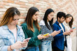 © Xavier Lorenzo - Group of friends using smart phones, standing against a brick wall, enjoying social media and mobile technology. Youth and technology lifestyle concept