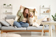 © Pixel-Shot - Young woman and cute Australian Shepherd dog with blanket sitting on sofa at home