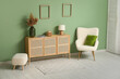 © Pixel-Shot - Wooden chest of drawers, soft armchair and pouf near green wall in room
