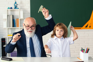 Fototapete - Happy kid in school break. Senior teacher with pupil with paper plane in school classroom. Education, elementary school. School break. Teacher with pupil with airplanes. Education concept.