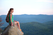 © bilanol - Sportive female hiker sitting alone taking a break on hillside trail. Lonely woman enjoying view of summer nature from rocky cliff on wilderness path. Active lifestyle concept