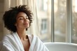 © Neha Snaps - a relaxed woman enjoying sunlight near the window in a bathroom setting. She is wearing a white robe and has her eyes closed, evoking peace and serenity
