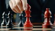 © Light of Art - A hand carefully moves a red chess queen piece into position on a chessboard du a strategic game of chess demonstrating planning and calculated moves.