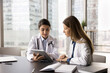 © fizkes - Interactive learning in medicine. Skilled millennial female doctor therapist physician mentoring teaching young girl student intern at clinic workplace explain medical problem on digital tablet screen