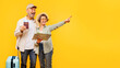 © Home-stock - Satisfied elderly husband and wife with map and passports posing on yellow studio background, pointing aside at free space. trip preparation, travel advertisement for retired