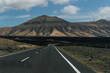 © Tina - A road leading to volcano on a volcanic island, under a blue sky dotted with clouds. Lanzarote
