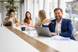 © Moon Safari - Businessman holding glasses and analyzing reports over laptop while sitting by female professionals in board room