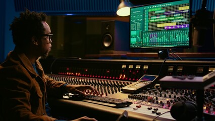 Leinwandbilder - Tracking engineer processing and mixing sounds in control room with audio console and professional editing software on computer. Music production expert uses motorized faders and knobs. Camera B.