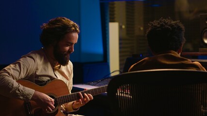 Leinwandbilder - Performer songwriter singing new tracks on his electro acoustic guitar and recording new music in post production. Musician working in collaboration with audio engineer in studio. Camera A.