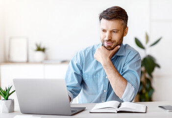 Aufkleber - Handsome Male Entrepreneur Using Laptop, Sitting At Desk In Home Office, Looking At Computer Screen With Pleased Face Expression, Having Business Ideas, Enjoying Working Remotely, Selective Focus