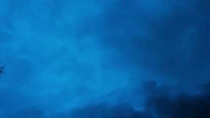 Wall Mural - fast moving timelapse of dark storm clouds passing overhead with blue hour sky. ominous cumulus clou