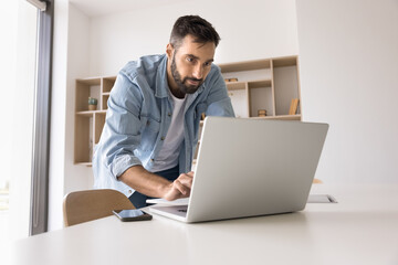 Concentrated young man leaning over work desk with notebook type message in chat write reply to email contact with colleague client online via social media manage important task solve business problem