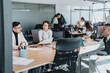 © qunica.com - A diverse group of business employees working together in an open-plan office. The team collaborates on documents and uses laptops, showcasing teamwork, communication, and a multicultural work