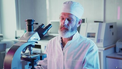 Wall Mural - experienced mature scientist wearing lab coat and cap performing precise microscope adjustment while