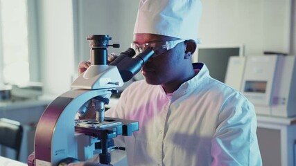 Wall Mural - focused black scientist in lab coat and safety glasses carefully analyzing biological samples using 