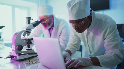 Wall Mural - two scientists, a senior caucasian man and a young african man, are working together in a modern lab