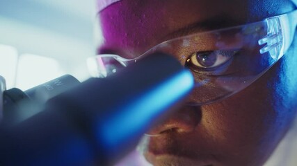 Wall Mural - close up of a scientist wearing safety glasses looking through a microscope, conducting research in 