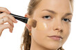 © vladimirfloyd - Close-up of young woman applying liquid foundation with makeup brush on cheek, showing smooth application process against white background
