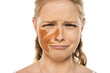 © vladimirfloyd - Young woman with worried, tearful expression showing distress over mismatched foundation streaks on face, demonstrating makeup mistake against white background