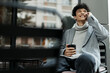 © SHOTPRIME STUDIO - Fashionable man sitting on a bench, talking on the phone and holding a coffee cup in front of his face while looking at the camera