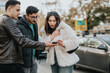 © qunica.com - Three friends engage in conversation while looking at a smart phone in an urban setting. They appear focused and connected, illustrating friendship, curiosity, and modern communication in a dynamic