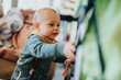 © qunica.com - A curious baby dressed in stylish attire interacts with a stroller indoors. The scene conveys a sense of discovery, joy, and everyday family life in a cozy home environment.