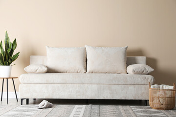 Poster - Comfortable sofa with pillows, houseplant and basket near beige wall