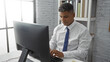 © Krakenimages.com - Young hispanic man working in an office typing on a computer wearing a white shirt and blue tie with a focused expression