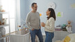 © Krakenimages.com - Middle aged hispanic couple standing in cozy bedroom smiling at each other near baby's cradle surrounded by soft toys and pastel decor, embodying love and family warmth.