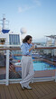© Krakenimages.com - Woman stands on a cruise ship deck enjoying a drink with a scenic ocean view, wearing sunglasses and relaxed attire, capturing a serene vacation moment outdoors at sunset.