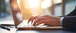 © YONG - Close-up of hands typing on a silver laptop keyboard, golden-hour sunlight streaming through window blinds onto a walnut desk.