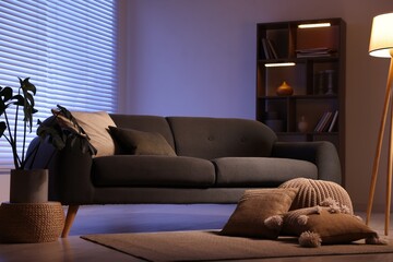 Poster - stylish living room with comfortable sofa and wooden shelving unit in evening. interior design