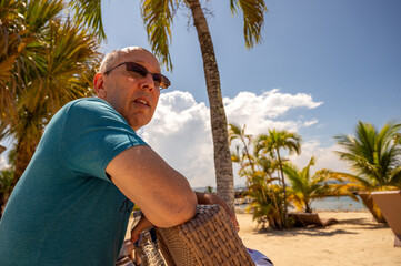 senior man in tropical beach paradise with palm trees blue sky