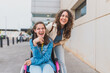 © Martí Rosselló - Young woman with cerebral palsy laughs with her personal assistant outdoors - They share a candid and joyful moment on the sidewalk - Concept of cerebral palsy