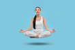 © New Africa - Young woman levitating during meditation on light blue background. Practicing yoga
