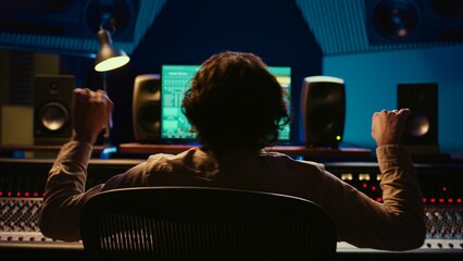 Leinwandbilder - Skilled sound designer enjoying his own music creating at mixing console in control room, feeling pleased with his new track. Audio expert editing tunes with knobs and sliders in studio. Camera B.