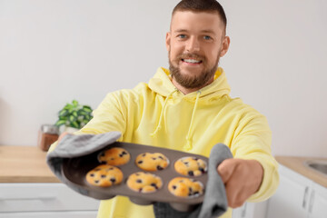 Wall Mural - young man holding baking dish with tasty muffins in kitchen