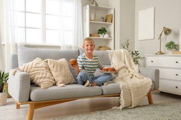 Wall Mural - little boy with tasty muffins sitting on sofa at home