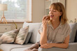 © Pixel-Shot - Young woman eating tasty muffin on sofa at home