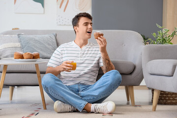 Wall Mural - young man with juice eating tasty muffin at home