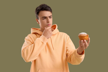 Wall Mural - thoughtful young man with tasty muffin on green background