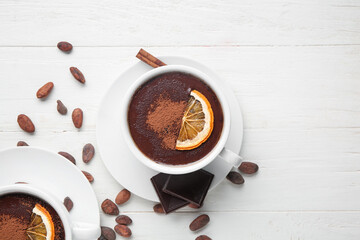 Wall Mural - cups of hot chocolate with cocoa beans and dried orange slices on white wooden background