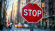 © Yoonnam - A modern, clean red stop sign with bold 'STOP' lettering stands on a city street, symbolizing traffic safety, awareness, control, and the importance of pausing in fast-paced urban life.