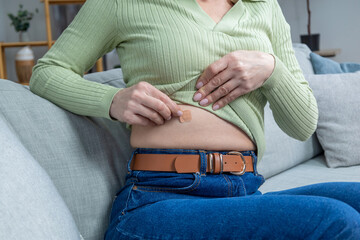 Woman in green shirt applying hormone replacement patch to her belly
