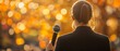 © santima - A speaker holds a microphone against autumn backdrop.
