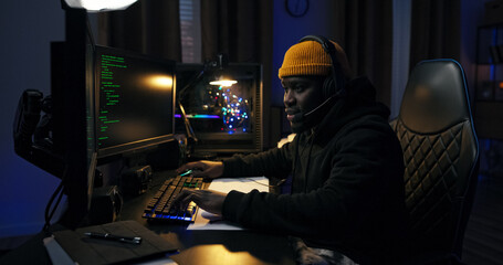 A young programmer begins his night shift at a remote job, entering a dark room lit by blue LED lights. He sits at his desk, puts on a headset, and starts a conversation with a colleague.