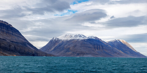Wall Mural - a panorama of the snow covered mountains and blue waters of geologfjord, in northeast greenland nati